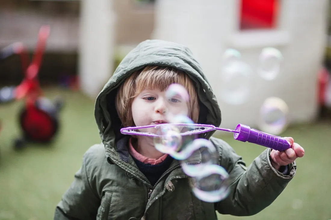 A child in a hooded coat blowing bubbles outdoors